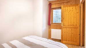 Un dormitorio con una puerta de madera, una ventana con cortina roja y un radiador.