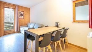 Una habitación acogedora con una mesa de comedor de madera, sillas negras, un sofá gris y una ventana con cortinas.