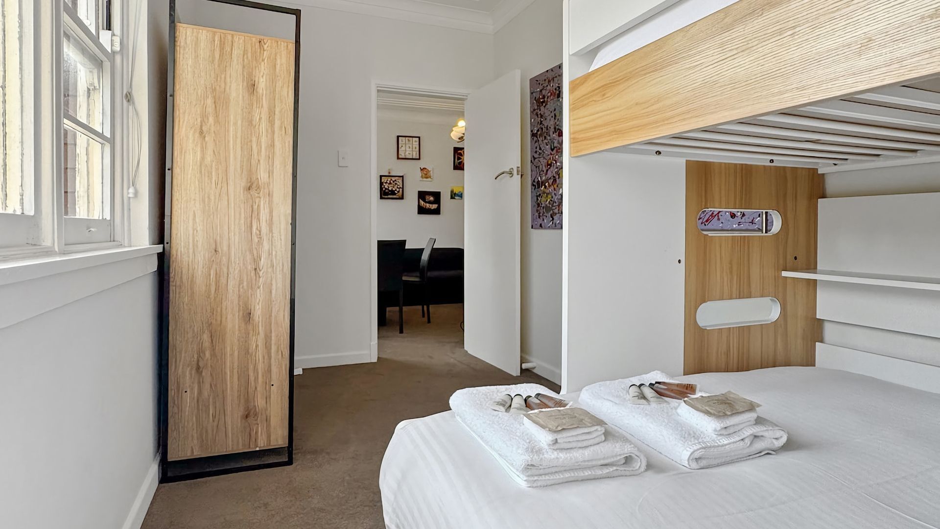 A hotel room with a bunk bed, a wooden door, a desk, and a chair.