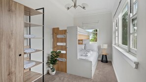 A compact bedroom with a bunk bed, a wooden wardrobe with shelves, a bedside plant, and a window with a view of greenery. - Warm Spacious Bondi Stay with Parking (Bondi)