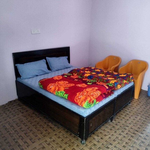 A bed with a floral bedspread, two pillows, and two orange chairs. - Aditya Guest House And Restaurant (Ukhimath)