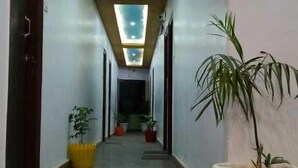 A long, narrow hallway with a polished floor, recessed lighting, and potted plants. - Hotel Mahaveer International (Varanasi)