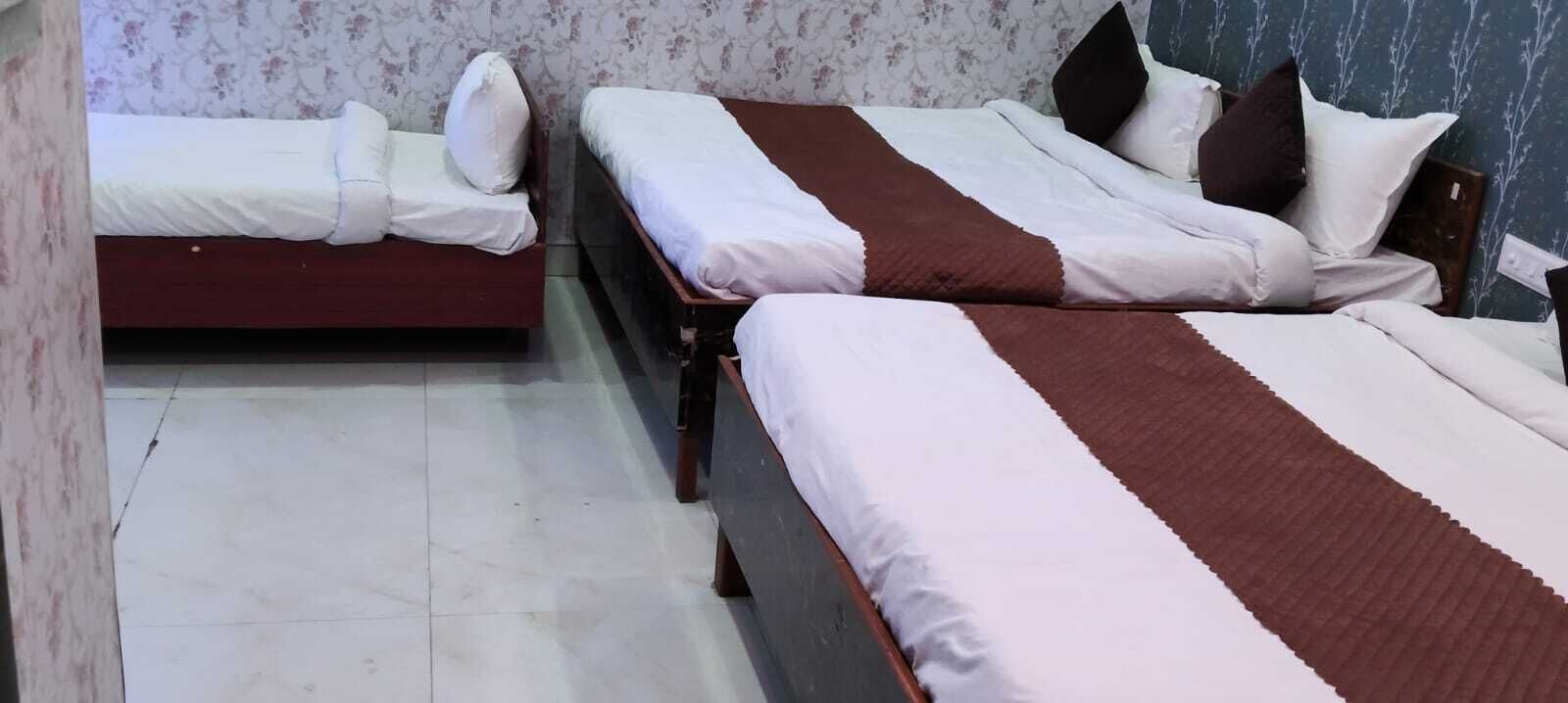 A room with two beds, each with white bedding and brown headboards. The walls have floral wallpaper, and the floor is tiled.