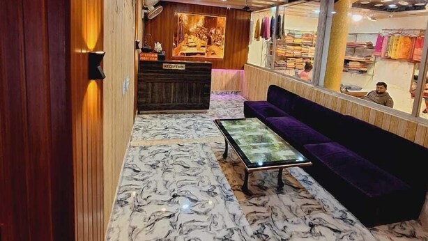 A hotel lobby with a reception desk, a seating area with a purple sofa, and a clothing store in the background. - Hotel Mahaveer International (Varanasi)