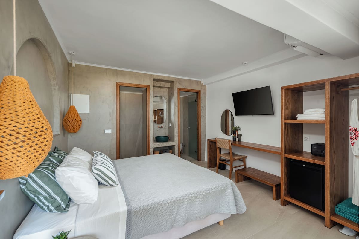A bedroom with a bed, wooden wardrobe, a desk, and a television.