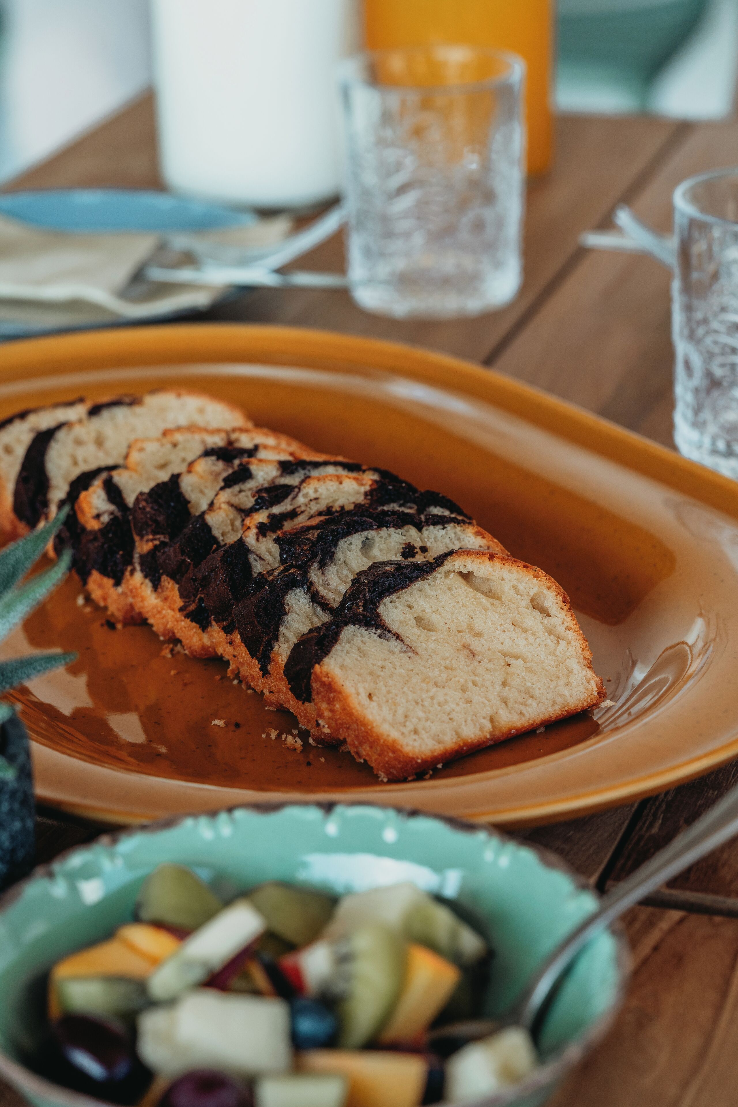 A slice of marble rye bread on a plate with a bowl of fruit in the foreground.