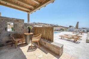 A rooftop terrace with stone walls, wicker chairs, a small table, and lounge chairs. - Athera  Suites  Mykonos (Mykonos)