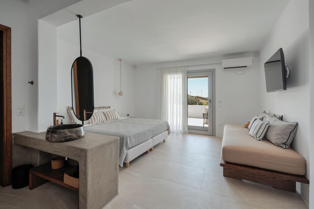 A modern bedroom with a bed, a sofa, a concrete sink, and a large window.