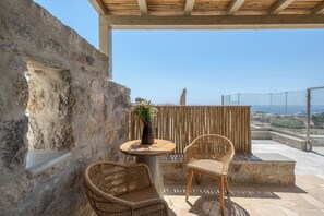 A balcony with stone walls, wicker chairs, a small table with a vase, and a view of the sea. - Athera  Suites  Mykonos (Mykonos)