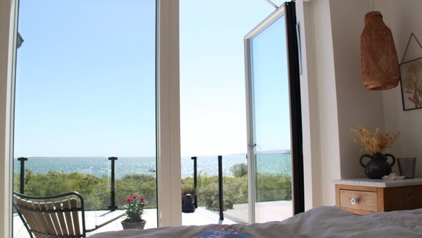 A bedroom with a large window overlooking a scenic view, a bed, a bedside table with a vase, and a chair. - "Valia" - 20m from the sea by Interhome (Sønder Stenderup)