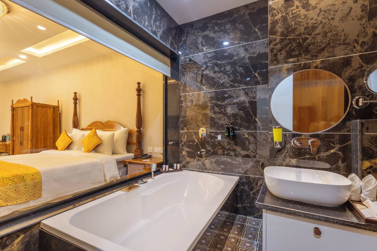 A modern hotel room with a large bed, a bathtub, and a marble bathroom.