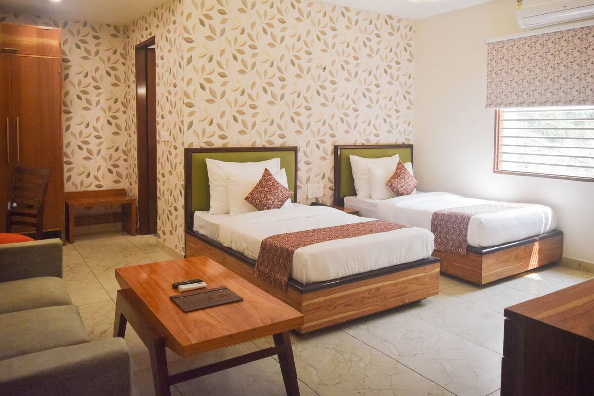 A hotel room with two beds, a wooden table, a sofa, and a wardrobe.