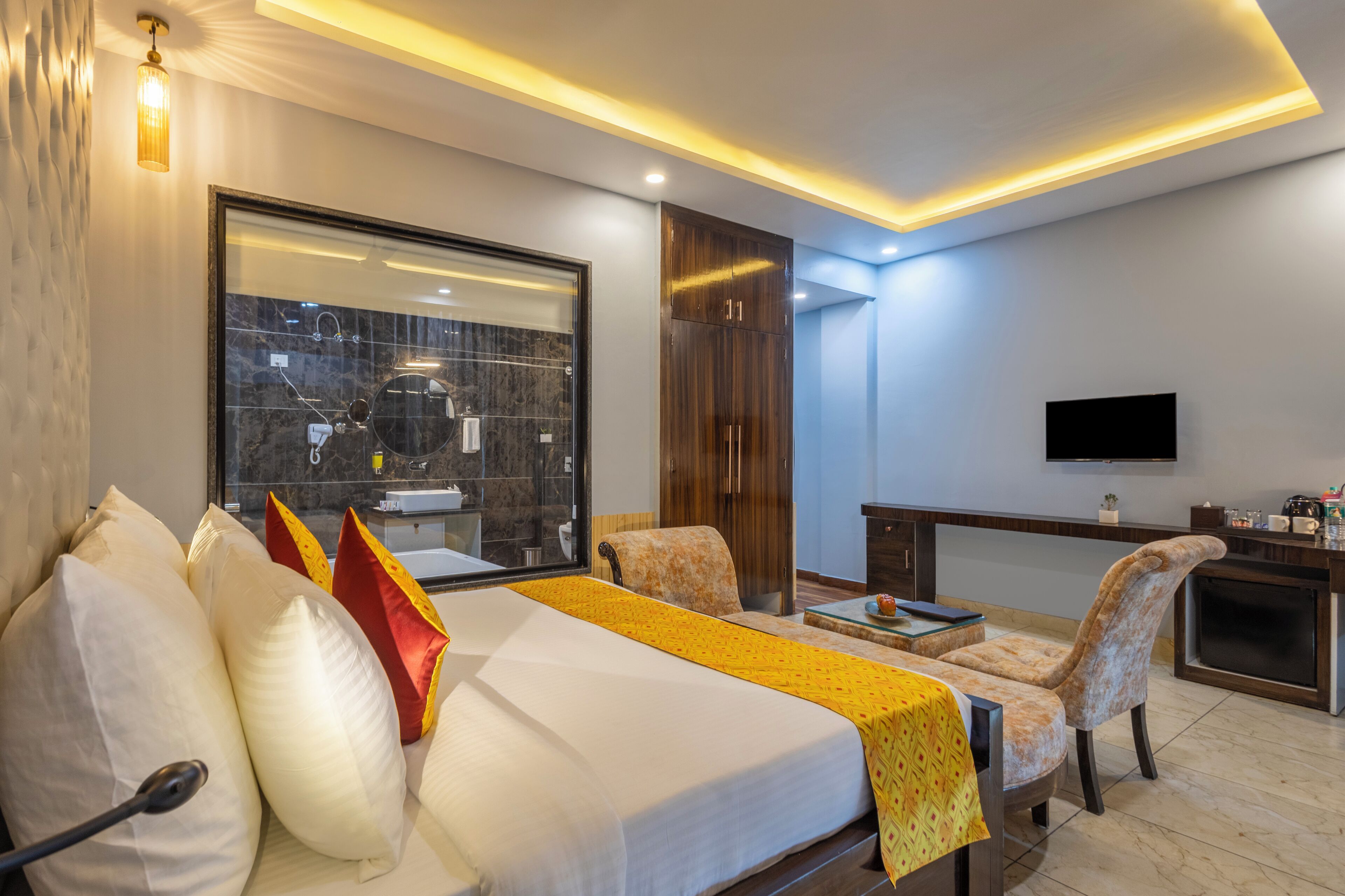 Habitación de hotel moderna con una cama grande, un escritorio, una silla, un televisor y un baño con cabina de ducha de vidrio.