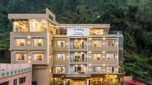 A multi-story hotel with a modern design, featuring balconies, a central entrance with a covered area, and a sign indicating the name and location. - Sterling Kastoori Rudraprayag (Jakholi)