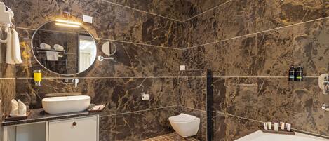 A modern bathroom with a large bathtub, a round sink, and a toilet.