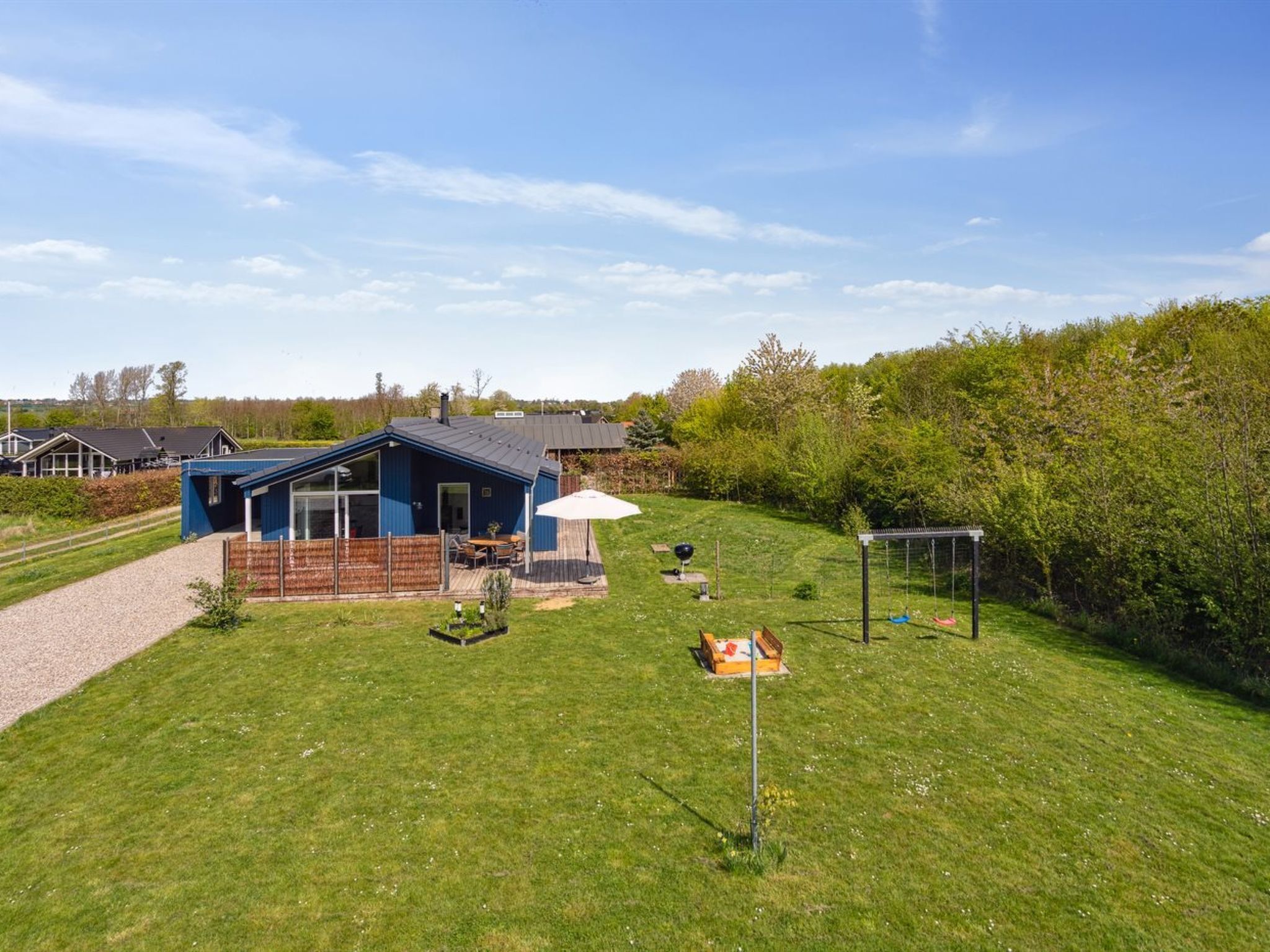 A blue house with a patio, a swing set, and a garden.