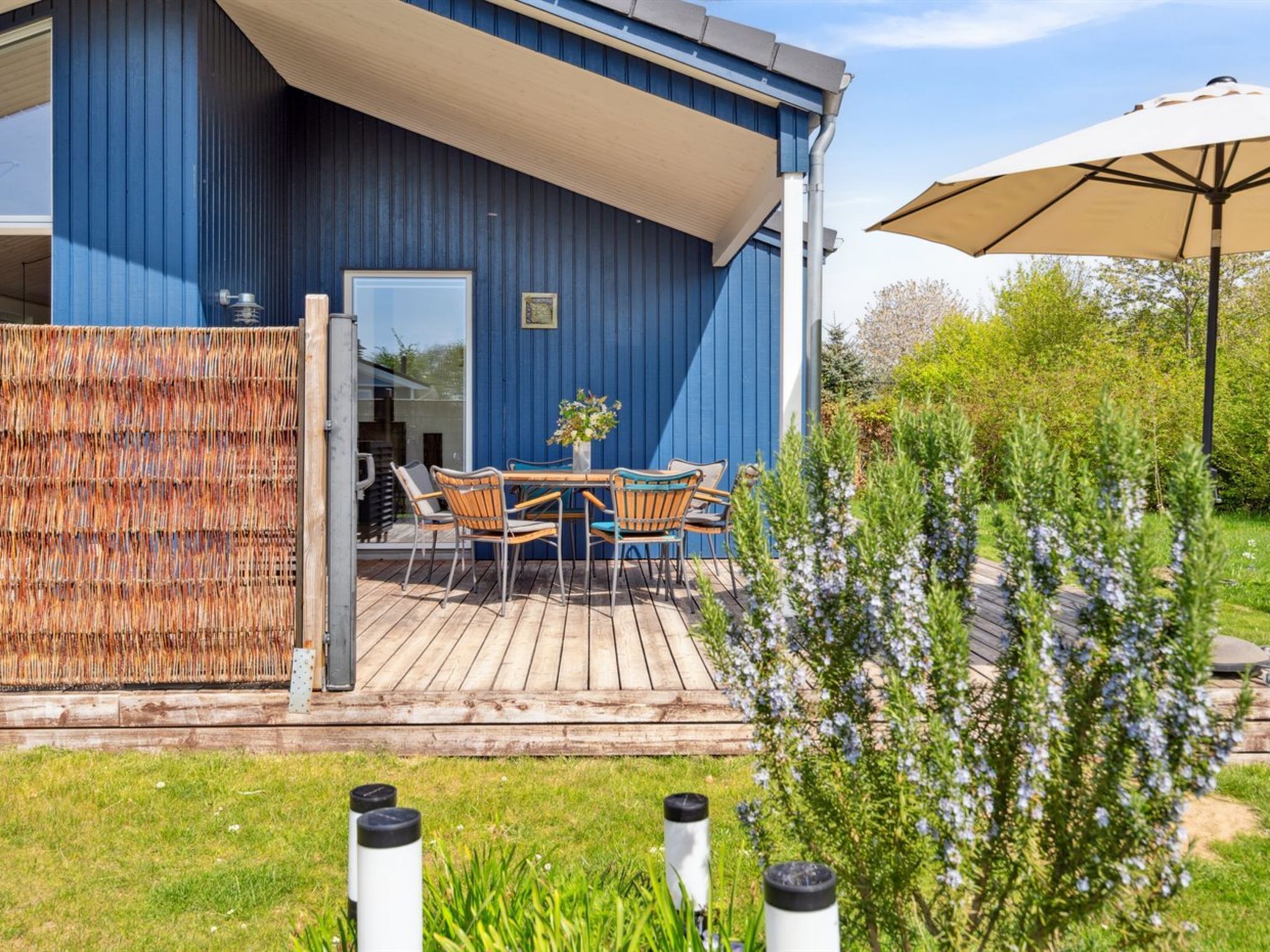 A blue building with a wooden deck, outdoor seating, and a garden area.