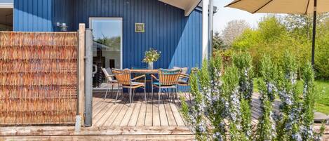 A blue building with a wooden deck, outdoor seating, and a garden area.
