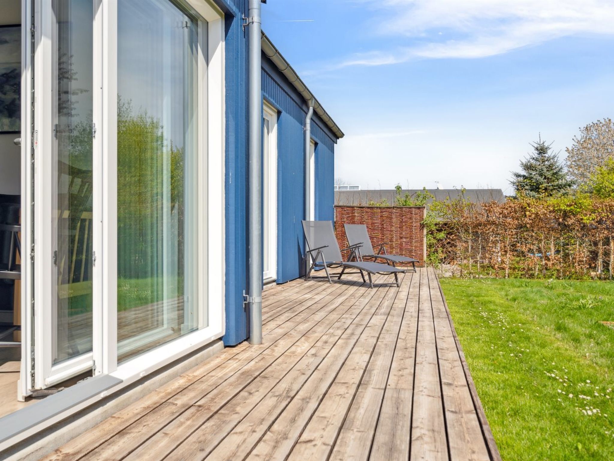 A modern house with large sliding glass doors, a wooden deck, and outdoor seating.