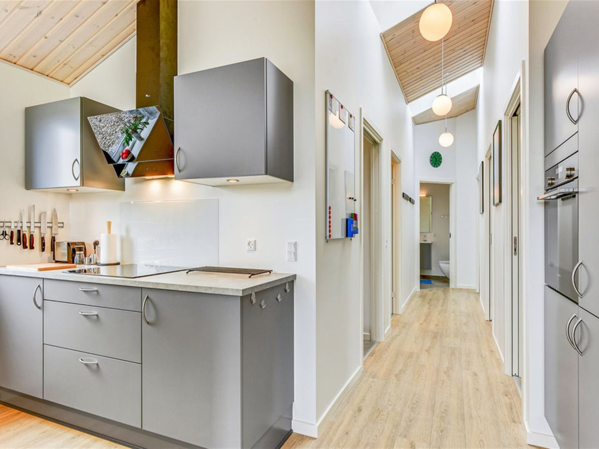 A modern kitchen with grey cabinetry, a central island, and a wooden ceiling.
