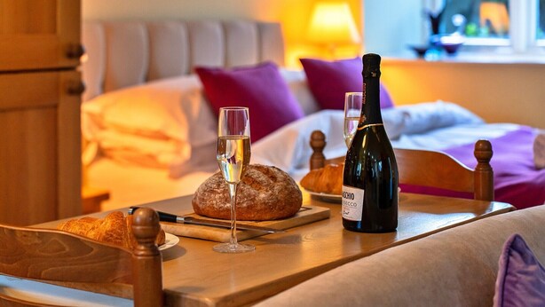 Una habitación acogedora con una cama, una mesa con vino, copas y pan.
