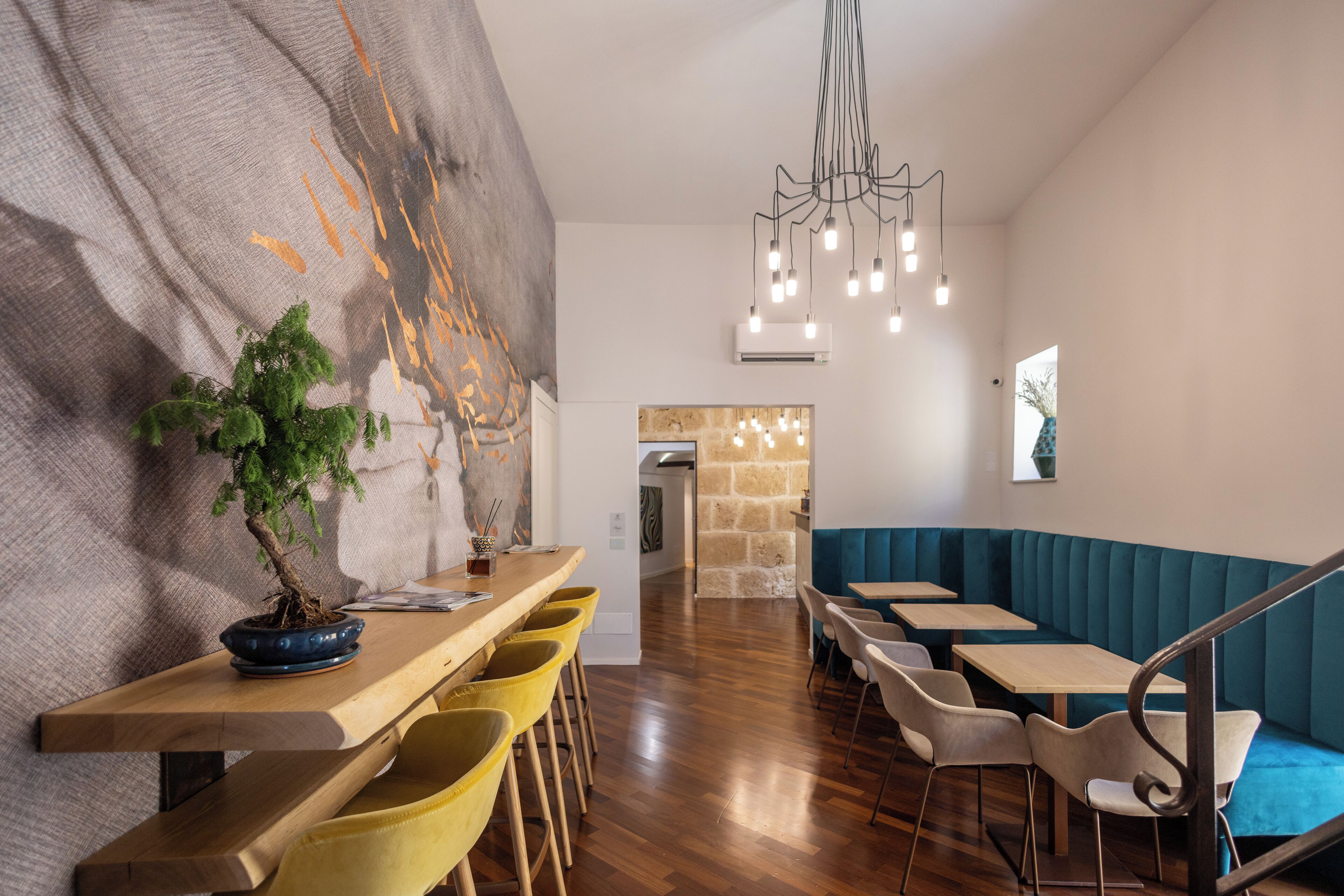 Un restaurante moderno con mesas de madera y sillas amarillas, un área de asientos en banco azul y un cuadro abstracto grande en la pared.