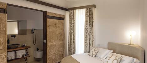 Un dormitorio moderno con una cama grande, suelo de madera, un armario empotrado, un baño con lavamanos y espejo, y una lámpara de techo circular.