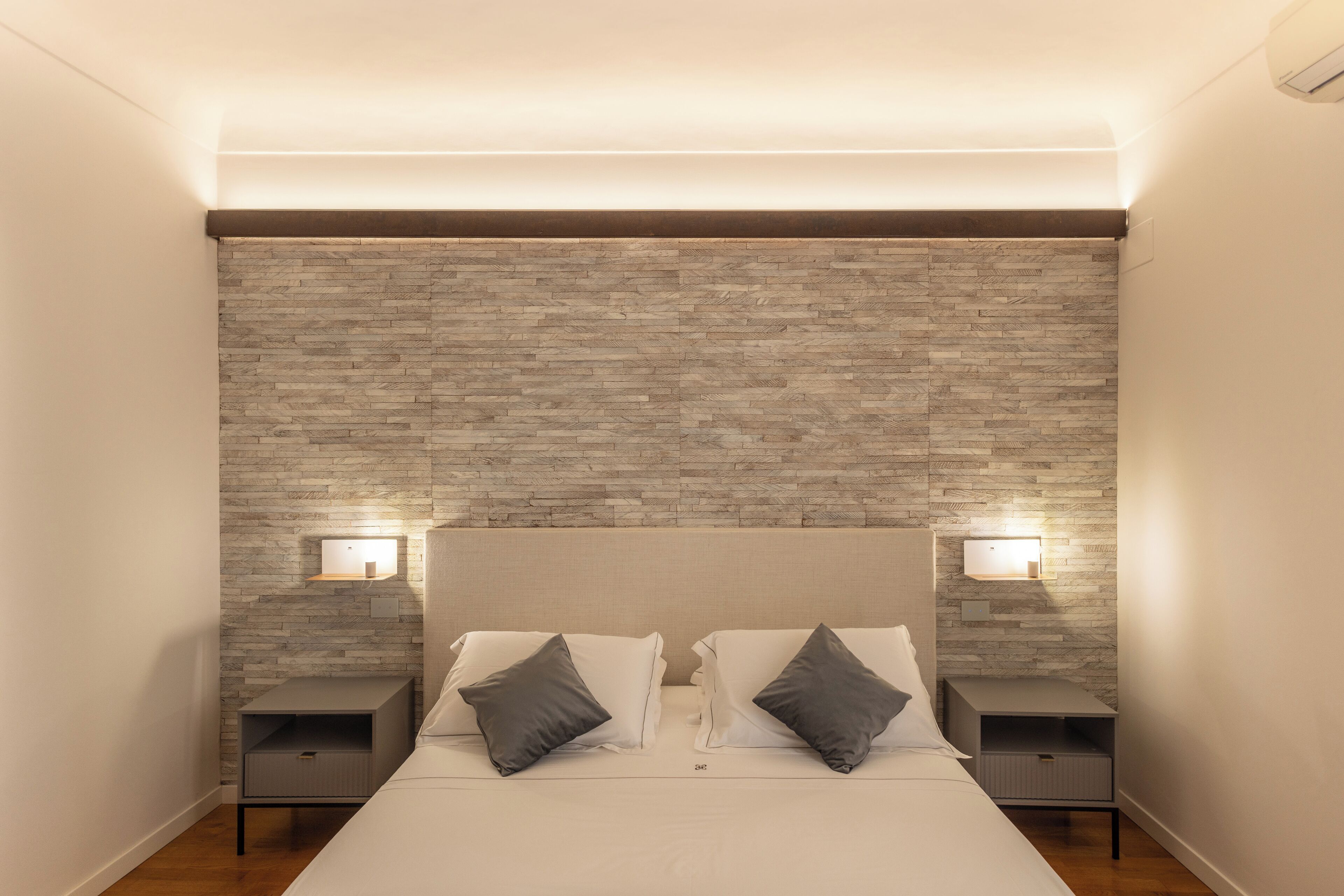 Un dormitorio ordenado con una cama, dos mesitas de noche y una pared con textura.
