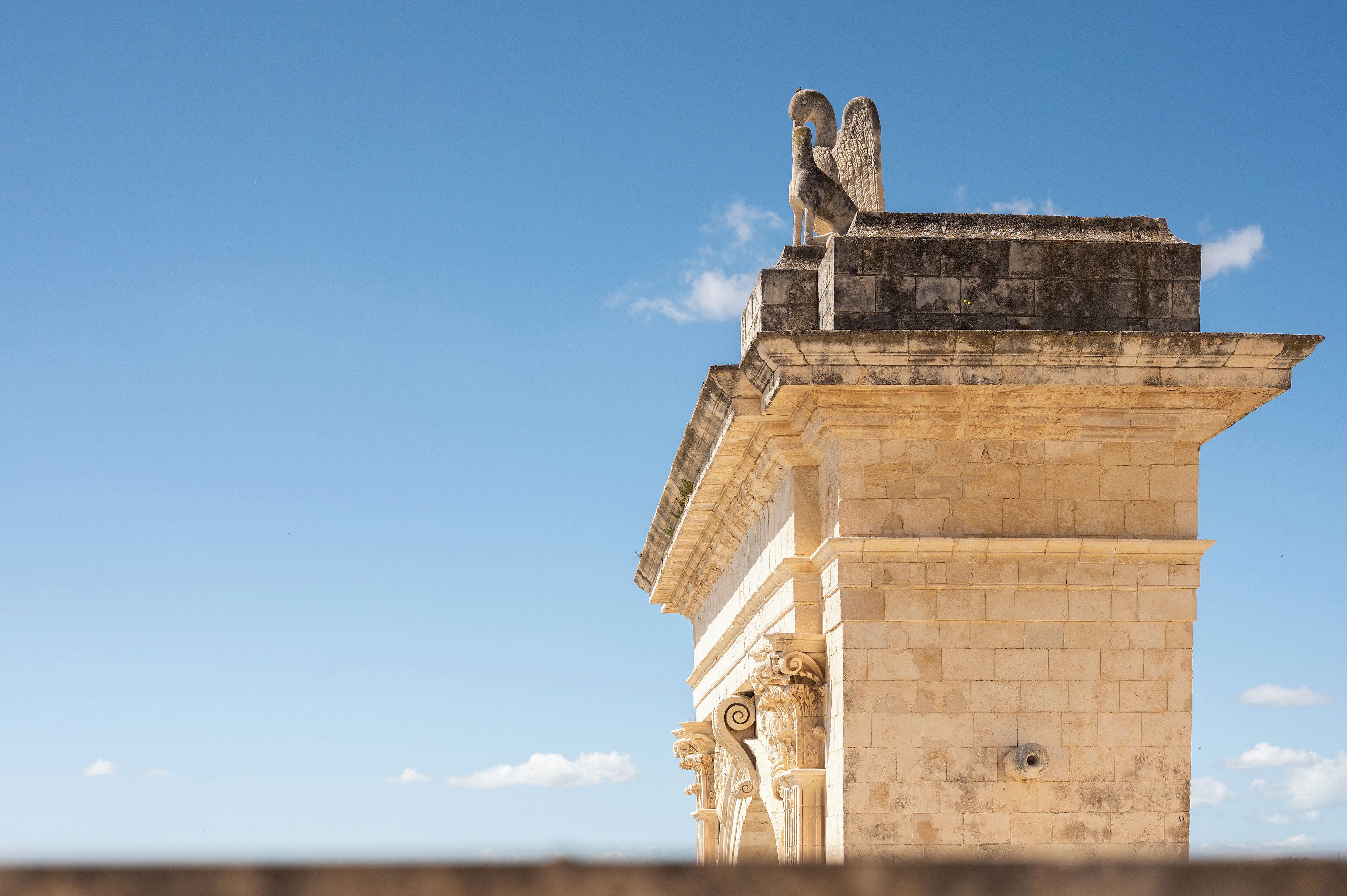 A stone structure with a bird sculpture on top, featuring classical architectural elements like columns and a detailed cornice.