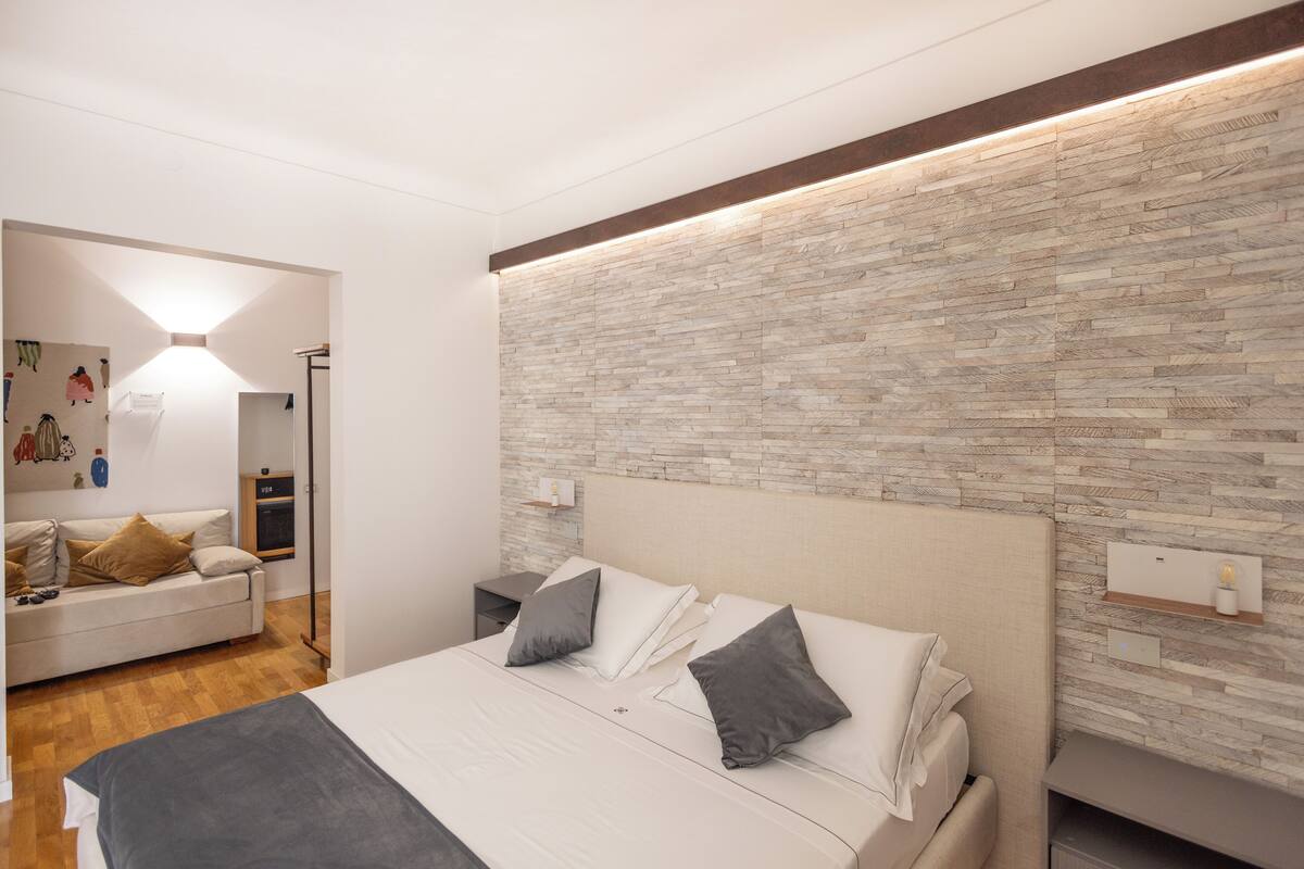 Un dormitorio moderno con una cama grande, una mesita de noche, un pequeño escritorio, una repisa en la pared y suelo de madera.