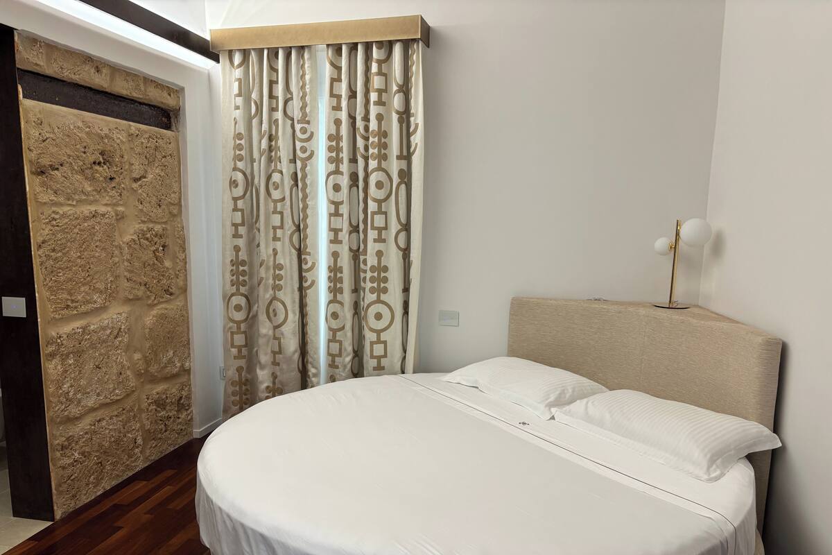 Un dormitorio con cama redonda, cabecera, pared con textura similar a la piedra y cortina con diseño geométrico.