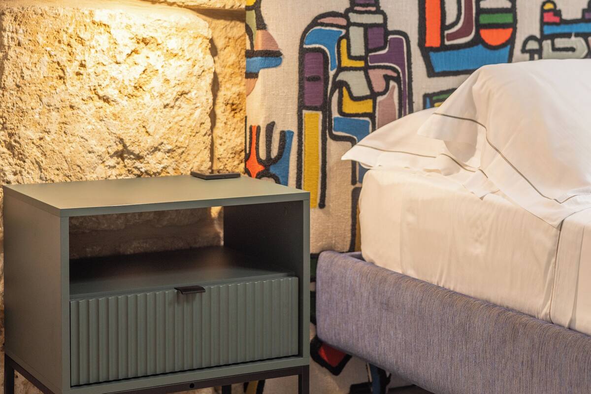 Una habitación con pared de piedra, un cuadro abstracto colorido, un armario gris y un sofá gris.