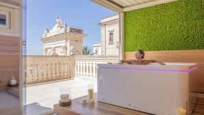 A spa area with a bathtub, candles, and a view of a historic building. - Noto Boutique Hotel (Noto)