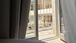 A room with a large window overlooking a courtyard with stone architecture and a bed. - Noto Boutique Hotel (Noto)