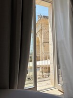 Una habitación con un ventanal grande que da a un patio con arquitectura de piedra y una cama.