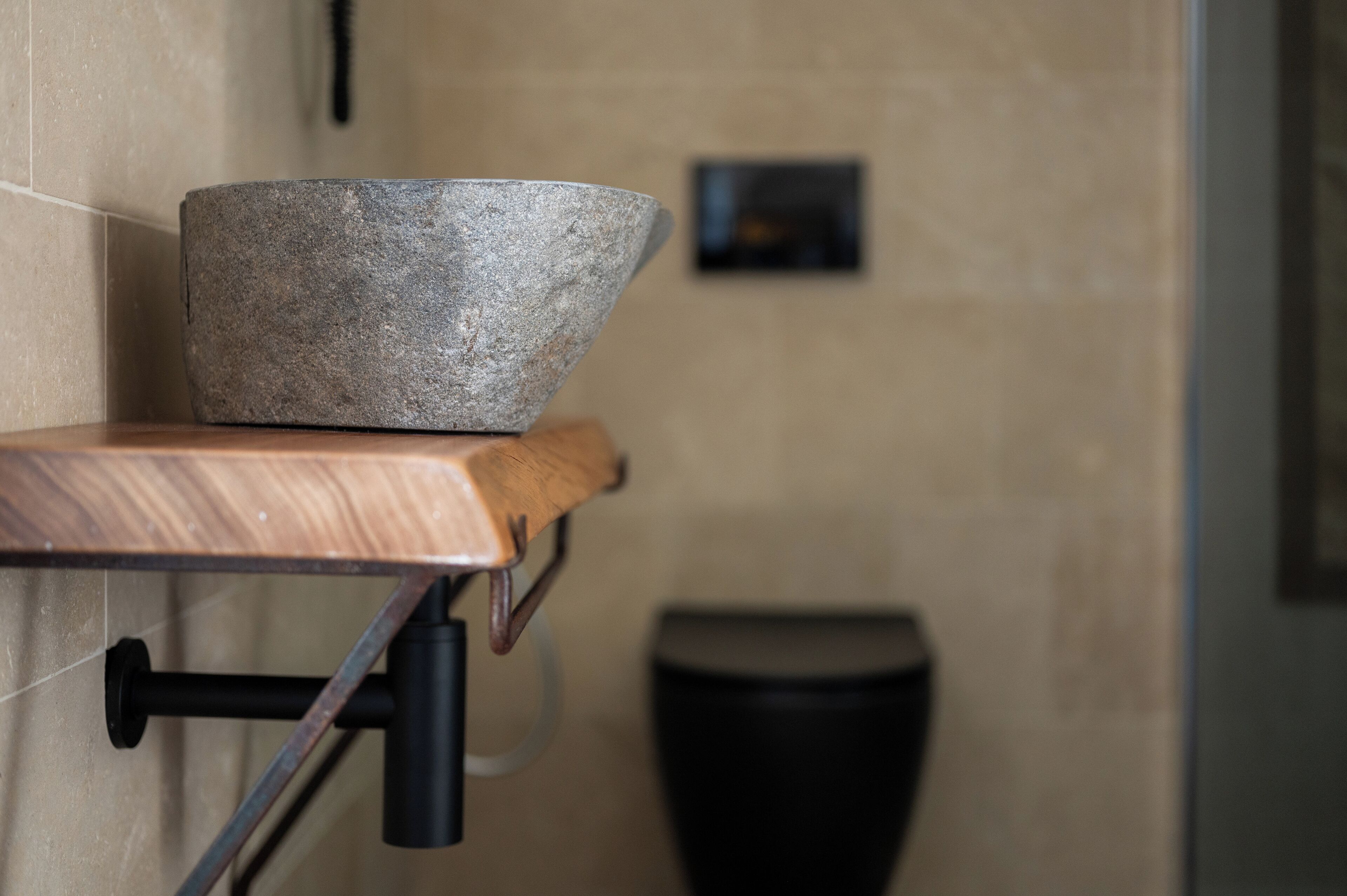 A stone bowl on a wooden ledge, a black trash bin, and a tiled wall.