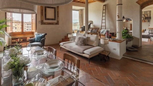 A cozy living room with a sofa, a dining table set for four, and a staircase leading to an upper level.