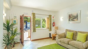 A living room with a sofa, a green rug, a lamp, a painting, and a window with curtains. - Monte Zest Apt in Lagos (Lagos)