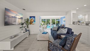 A modern living room with a large TV, a sofa, a coffee table, and a view of a pool and outdoor area.