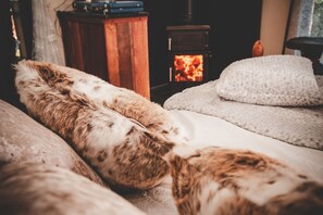 A cozy room with a bed, a fluffy pillow, a blanket, and a wood-burning stove in the background. - Treehouse in Germansweek near Dartmoor Trails (Germansweek)