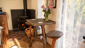 A rustic room with a wooden table, a bench, a vase with flowers, a fireplace, and a checkered floor. - Treehouse in Germansweek near Dartmoor Trails (Germansweek)