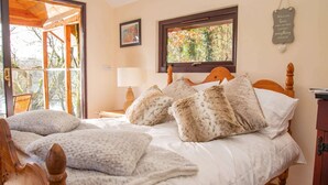 A bedroom with a wooden bed, white bedding, and a window with a view of trees. - Treehouse in Germansweek near Dartmoor Trails (Germansweek)
