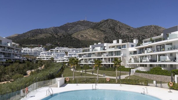 Un moderno resort con piscina, edificios blancos y montañas al fondo.