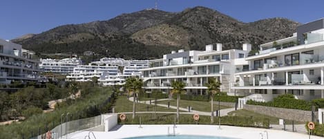 Een modern resort met een zwembad, witte gebouwen en een bergachtig achtergrond.