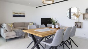 Un comedor moderno con una mesa de madera y sillas tapizadas de gris, un sofá gris y un espejo grande en la pared.