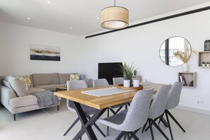 A modern dining area with a wooden table and grey upholstered chairs, a grey sofa, and a large mirror on the wall.