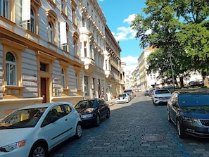 Mukulakivikatu, jonka varrella on historiallisia rakennuksia, parkkeerattuja autoja ja puita.