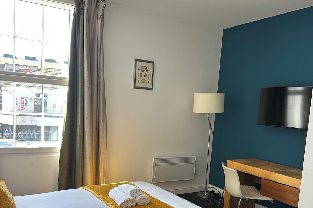 Hotellihuone, jossa on sänky, työpöytä, tuoli, televisio ja ikkuna, jossa on verhot.