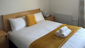 Una cama bien hecha con ropa de cama blanca y color mostaza, un cabecero de madera y una manta amarilla.
