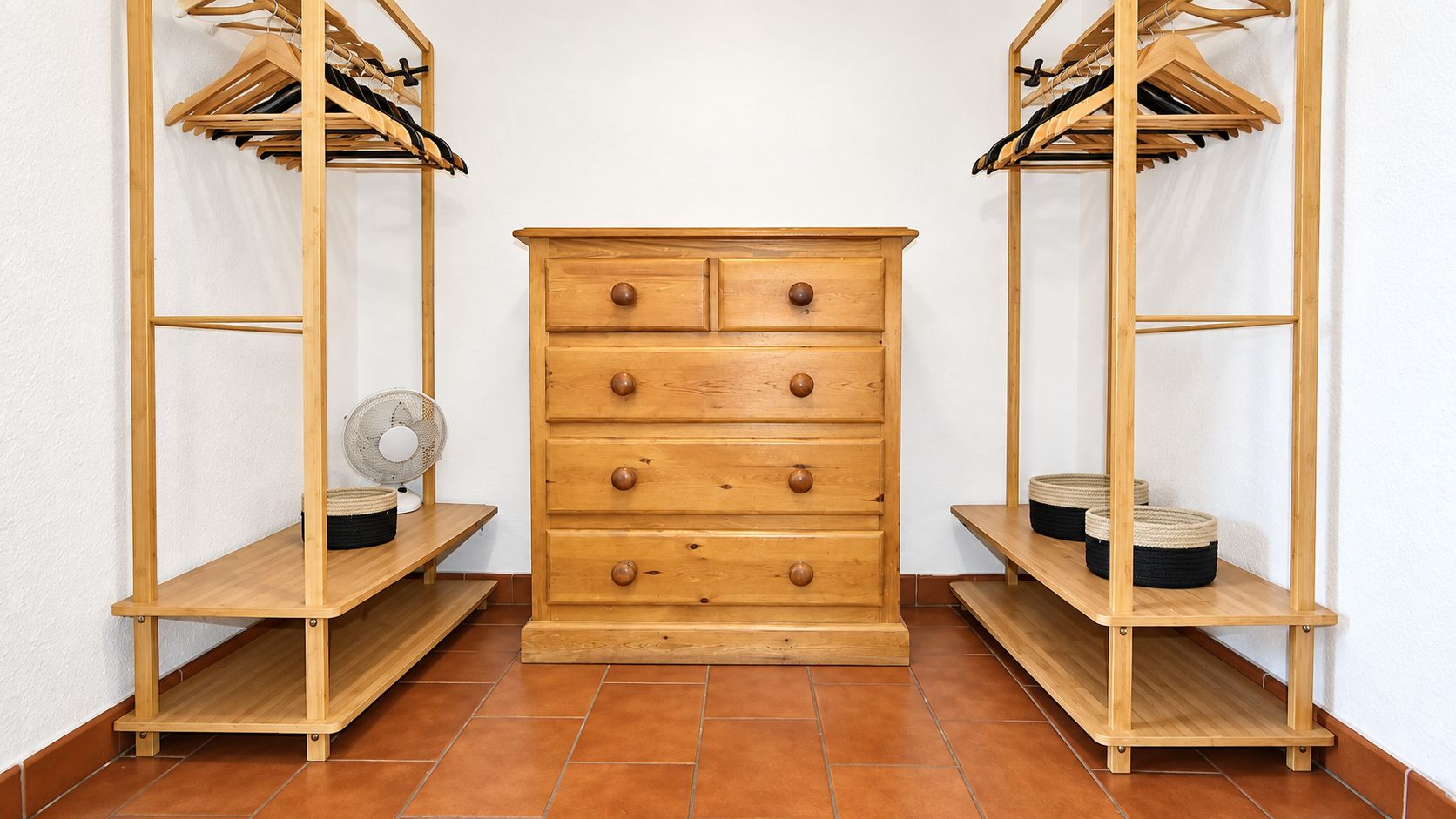 A wooden dresser with drawers and a fan on a shelf, flanked by wooden shelving units with baskets.